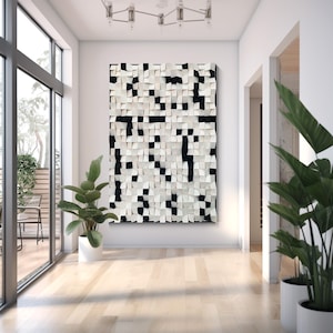 May include: A large, abstract wall art piece with a textured surface. The artwork features a pattern of white and black square blocks, creating a pixelated effect. The piece is mounted on a white wall in a modern interior setting, with plants and natural light.