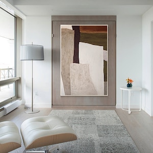 May include: Abstract art painting with brown, white, and green geometric shapes on a canvas. The painting is hanging on a wall in a modern living room.