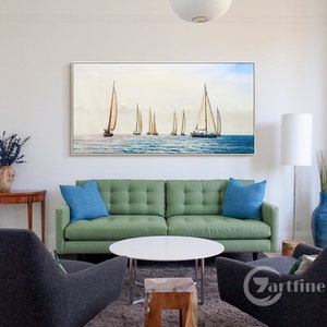Pode incluir: Uma pintura emoldurada de veleiros em um corpo de &aacute;gua. A pintura est&aacute; pendurada em uma parede branca acima de um sof&aacute; verde com almofadas azuis. H&aacute; uma mesa de centro branca na frente do sof&aacute;.