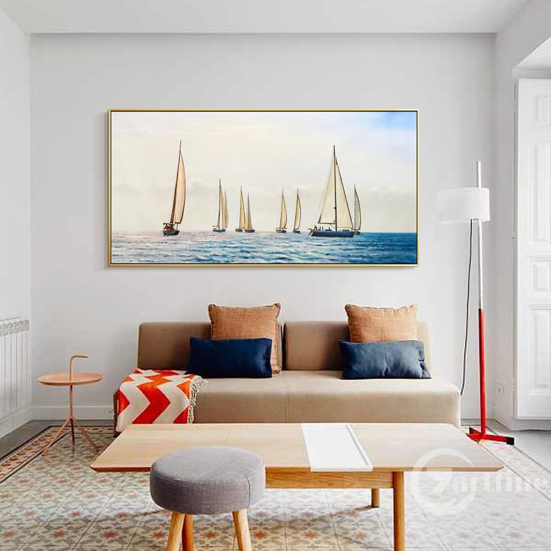 Pode incluir: Uma impress&atilde;o em tela emoldurada de uma paisagem mar&iacute;tima com veleiros em um mar azul calmo. A impress&atilde;o est&aacute; em um ambiente de sala de estar com um sof&aacute;, uma mesa de caf&eacute; e um abajur.