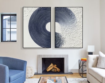 May include: Two framed abstract wall art pieces. One features a navy blue concentric circle design, the other a textured white and navy blue design. The art hangs above a fireplace in a living room setting.