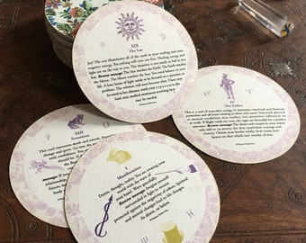 Könnte beinhalten: Ein Satz von 10 runden Tarotkarten mit bunten Illustrationen und Text. Die Karten sind auf weißem Hintergrund mit rosa Rand gedruckt. Die Karten zeigen verschiedene Symbole, darunter die Sonne, ein Kaninchen, ein Frosch und ein Mann mit einem Schwert. Der Text auf den Karten enthält die Namen der Karten, wie z. B. "Die Sonne", "Übergang", "Manifestation" und "Der Vater".