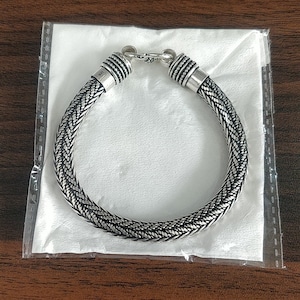 Puede incluir: Un brazalete trenzado de plata con cierre de broche. El brazalete est&aacute; hecho de un dise&ntilde;o de metal tejido.