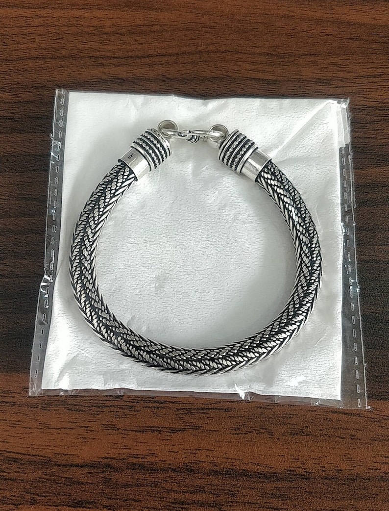 Puede incluir: Un brazalete trenzado de plata con cierre de broche. El brazalete est&aacute; hecho de un dise&ntilde;o de metal tejido.
