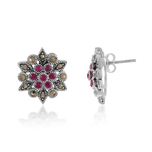 May include: A pair of silver earrings with a floral design. The earrings are adorned with small pink gemstones and gray marcasite stones.