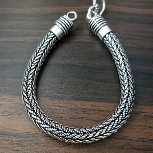 Puede incluir: Un brazalete de plata con un dise&ntilde;o trenzado. El brazalete tiene un cierre de broche.