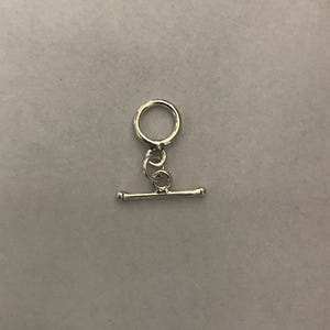 Może przedstawiać: Srebrna klamra zamykana z okrągłym pierścieniem i przesuwanym prętem. Ten rodzaj zapięcia jest używany do naszyjników, bransoletek i innych ozdób.