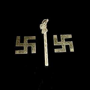 Könnte beinhalten: Ein Set aus drei silberfarbenen Metallgegenständen, bestehend aus zwei quadratischen Plaketten mit geprägtem Swastika-Symbol und Blumenmustern sowie einem langen, schlanken, vertikalen Stab mit einem pfauenartigen Motiv.