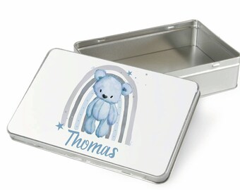 May include: A rectangular metal tin with a lid. The lid features a blue teddy bear illustration with a rainbow and the name "Thomas" in blue script. The tin is silver in color.