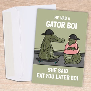 May include: A greeting card with a light green background and the text "HE WAS A GATOR BOI SHE SAID EAT YOU LATER BOI". The card features cartoon alligators wearing hats and shirts. A white envelope is next to the card.
