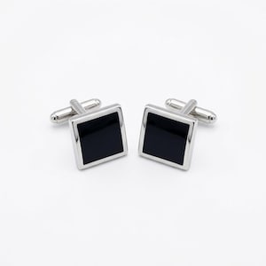 May include: A pair of silver cufflinks featuring a square black enamel centre. The cufflinks have a classic design, suitable for formal occasions. The black enamel is framed by polished silver.