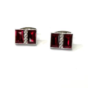 May include: A pair of silver cufflinks with red and clear rectangular stones. The stones are set in a silver frame.