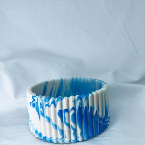 May include: A white and blue marbled ceramic bowl with a fluted rim. The bowl is round and has a smooth, glossy finish.