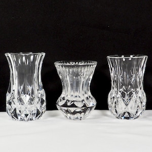 May include: Three clear glass bud vases with a diamond pattern. The vases are different sizes and are arranged in a row on a white surface.