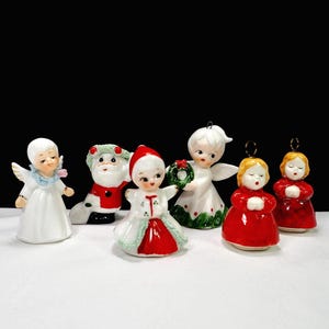 Puede incluir: Una colecci&oacute;n de adornos navide&ntilde;os vintage. Los adornos incluyen &aacute;ngeles, una figura de Pap&aacute; Noel y figuras con vestidos rojos y blancos. Los adornos son de cer&aacute;mica y tienen un acabado brillante. Los &aacute;ngeles tienen alas blancas y halos.