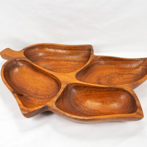 May include: A wooden serving tray with four separate compartments, shaped like a leaf. The tray is made of dark brown wood and has a natural finish.