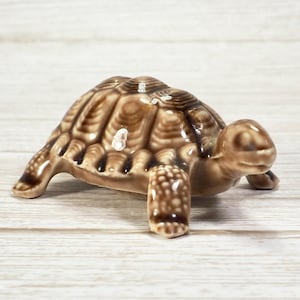 May include: A ceramic turtle figurine in shades of brown. The turtle has a detailed shell pattern and is posed with its legs extended. The figurine is a decorative item, likely for display.