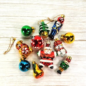 May include: A collection of assorted glass Christmas ornaments including a nutcracker, a Santa Claus figure, a snowman, a bear holding a candy cane, a green Christmas tree, a pear, and several round spheres in red, green, blue, and gold colors.