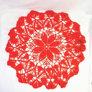 May include: A handmade, red crocheted doily with a floral design. The doily features a central flower pattern surrounded by intricate openwork and a scalloped edge. The bright red color and detailed craftsmanship make it a decorative piece.