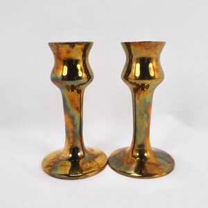 May include: A pair of gold-toned ceramic candle holders with a flared base and a smooth, shiny finish.