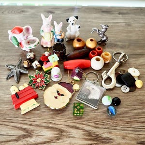 May include: A collection of small decorative items including figurines of animals, Christmas ornaments, a Santa Claus pin, a keychain with an eagle, buttons, and marbles. The items are arranged on a wooden surface.