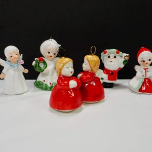 Puede incluir: Una colecci&oacute;n de adornos navide&ntilde;os vintage. Los adornos incluyen &aacute;ngeles, una figura de Pap&aacute; Noel y una ni&ntilde;a con un vestido rojo y blanco. Los adornos son de cer&aacute;mica y tienen detalles dorados. Los &aacute;ngeles tienen alas y vestidos blancos.