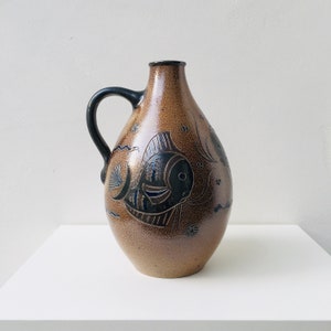 Peut inclure: Un pichet en céramique brun avec une anse noire et un motif de poisson bleu et brun.