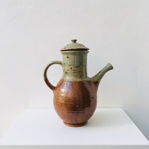 Op de afbeelding: Een bruine en grijze keramische theepot met een deksel. De theepot heeft een gespikkeld glazuur en een rond lichaam.