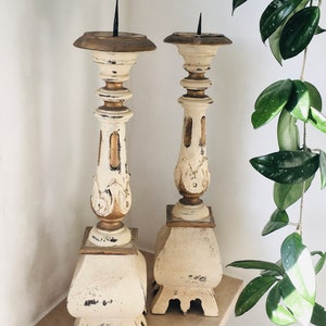 Può includere: Un paio di candelabri alti in legno bianco con dettagli dorati. I candelabri hanno una finitura anticata e un design decorativo.