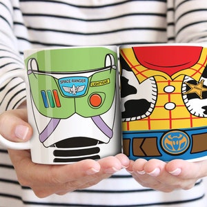Puede incluir: Dos tazas de cer&aacute;mica blanca con dise&ntilde;os de personajes. Una taza presenta un dise&ntilde;o verde y blanco de Buzz Lightyear con las palabras "Space Ranger" y "Lightyear". La otra taza tiene un dise&ntilde;o de Woody con una camisa amarilla, pa&ntilde;uelo rojo y placa de sheriff.