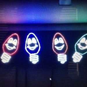 May include: Four light-up Christmas decorations shaped like light bulbs with smiling faces. The bulbs are red, blue, red, and green.