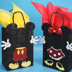 Könnte beinhalten: Zwei schwarze Geschenktüten, die mit Mickey Mouse und Minnie Mouse Figuren verziert sind. Die Mickey Mouse Tüte hat gelbes Seidenpapier im Inneren und die Minnie Mouse Tüte hat rotes Seidenpapier im Inneren.