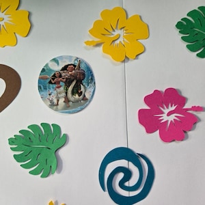 Pode incluir: Um conjunto de decora&ccedil;&otilde;es para festas com tema Moana, incluindo folhas verdes e marrons, flores de hibisco rosa e amarelas, um design de espiral azul e duas imagens redondas de Moana e Maui.