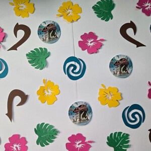 Pode incluir: Uma cole&ccedil;&atilde;o de decora&ccedil;&otilde;es para festas com tema Moana, incluindo recortes de papel de flores, folhas e o gancho do personagem Maui. H&aacute; tamb&eacute;m redemoinhos de papel azul e verde e recortes de papel redondos com imagens de Moana e Maui.