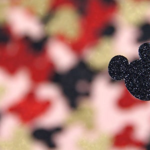 May include: A black glitter Mickey Mouse head cutout against a blurred background of red, pink, and gold glitter.