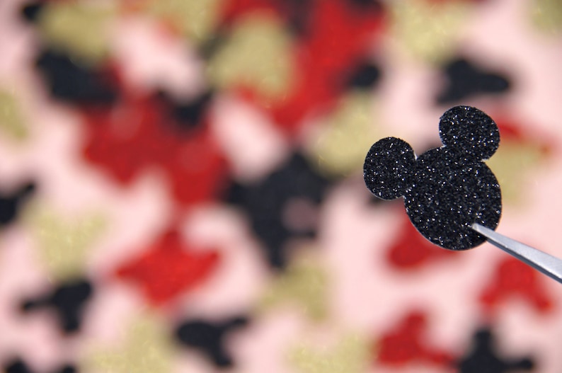 May include: A black glitter Mickey Mouse head cutout against a blurred background of red, pink, and gold glitter.