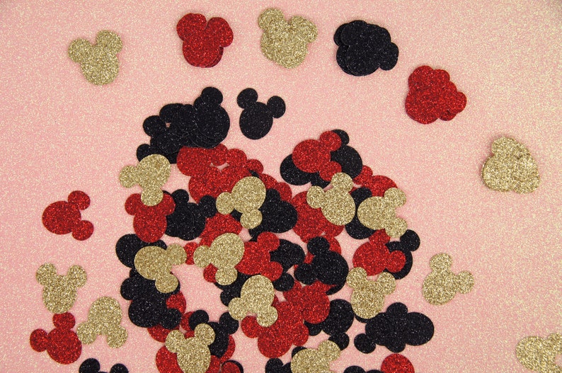 May include: A scattering of red, gold, and black glitter Mickey Mouse head confetti on a pink background.