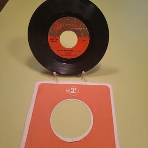 May include: A black vinyl record with a white label. The label has the text "The Electric Prunes" and "I Had Too Much To Dream" on it. The record is on a red and white paper sleeve with the text "Reprise Records" and "Printed in U.S.A."