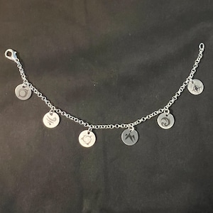May include: A silver chain bracelet with six silver charms, each featuring a different symbol. The charms are round and have a slightly raised design.