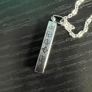 May include: A silver necklace with a rectangular pendant featuring five geometric symbols engraved on it.