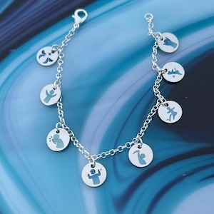 May include: A silver charm bracelet with multiple round charms. Each charm features a blue design of a person in various poses. The bracelet has a lobster clasp closure and is displayed on a blue surface.