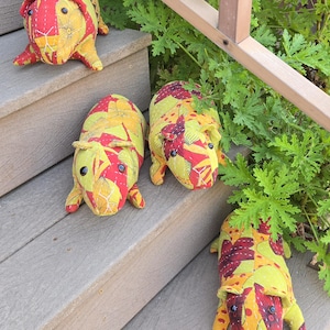 May include: Several handmade guinea pig plush toys in yellow, red, and orange floral fabric are arranged on wooden steps. The plushies have small black eyes and are in various poses, some with their legs extended.
