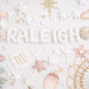 May include: A decorative banner spelling "RALEIGH" in white felt letters, surrounded by felt stars, clouds, and sea-themed elements. The design includes a gold glitter star, a pink fish, and a woven mirror.