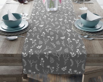 May include: A gray table runner with a white floral pattern. The runner is on a wooden table with two place settings on each side.