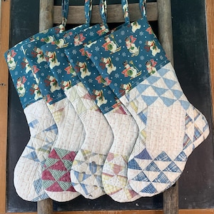 May include: Five quilted Christmas stockings featuring a teal cuff with a repeating snowman pattern. The lower sections are constructed from various patchwork fabric squares in shades of blue, pink, green, and yellow, each with a hanging loop.