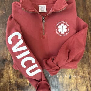 May include: A maroon quarter-zip sweatshirt with the text "CVICU" in white on the left sleeve and a white logo with the text "Cardiovascular Intensive Care Unit" on the front.