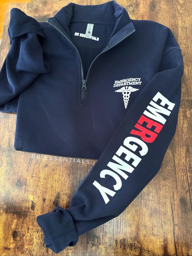 May include: Navy blue 1/4 zip sweatshirt with the text "ER Essentials" on the front and the text "EMERGENCY" on the sleeve in white with a red "E". The back of the sweatshirt has a white medical symbol with the text "EMERGENCY DEPARTMENT" above it.