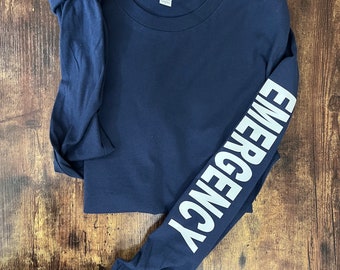 May include: A navy blue long-sleeve t-shirt with the word "EMERGENCY" printed vertically in white on the left sleeve.