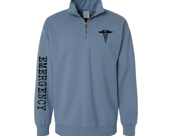 May include: A blue 1/4 zip sweatshirt with the words "EMERGENCY" printed on the left sleeve and a medical caduceus symbol on the right chest. The sweatshirt is made by ER Essentials.