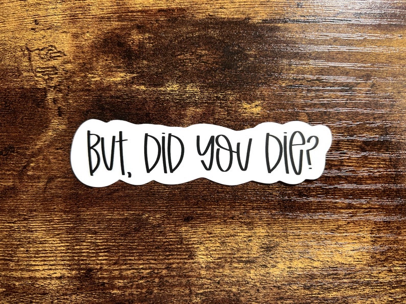 May include: White sticker with black text that reads "But, did you die?" on a brown wooden background.
